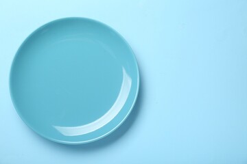 Empty ceramic plate on light blue background, top view. Space for text