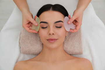 Fototapeta na wymiar Young woman receiving facial massage with gua sha tools in beauty salon, top view
