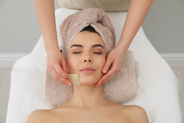 Young woman receiving facial massage with gua sha tool in beauty salon, top view