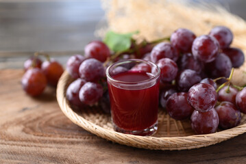 Red grape and juice in glass on wooden background, healthy drink