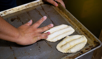 Man baker's hands making the bobbin shape. Baker making bread on a tray.