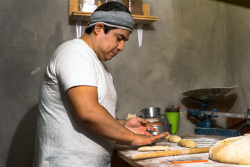Latin male baker kneads dough on wooden table