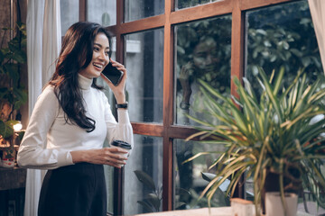 young businesswoman talking on the phone about the success of the business. Woman talking on the phone and smiling near the window at the cafe.