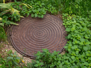 Iron manhole of the city sewer. A rusty manhole on a concrete base closes the entrance to the sewer lines. City sewer system.