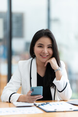 Obraz na płótnie Canvas Asian businesswoman in formal suit in office happy and cheerful during using smartphone and working.