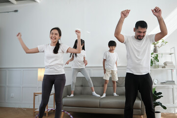 Happy wellness Asian Thai family, parents, and children are fun playing hula hoops together, fitness training and healthy exercise in white living room, domestic home lifestyle, and weekend activity.