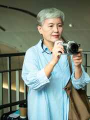 Portrait of happy senior adult elderly asia woman 60s taking pictures with photo camera for travel concept.