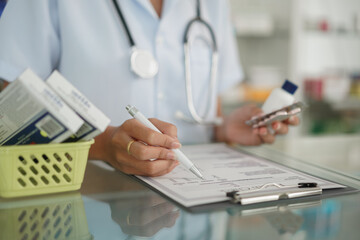 Medicine and health concept, Female pharmacist hold pill bottle and capsule to writing prescription