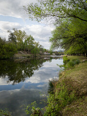 Río en el bosque con construcciones al fondo. Reflejos en el agua.