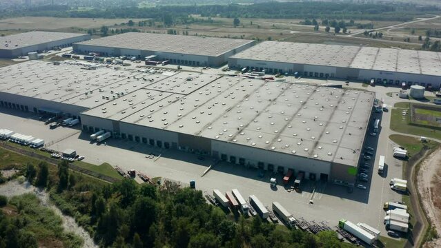 Drone shot on a logistics park with a warehouse - a loading hub. Semi-trailers stand on ramps for loading, unloading goods at sunset. Goods distribution warehouse. Semitrailers load cargo containers.