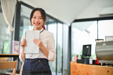 Smiling Asian female barista or waitress in a uniform holding portable tablet