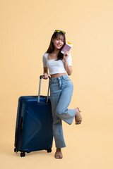 Young attractive Asian woman traveler wearing sunglasses standing with luggage, passport and boarding pass ticket isolated on yellow background, Tourist girl having cheerful holiday trip concept