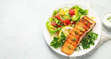 Salmon steak with vegetables and fries on light background.