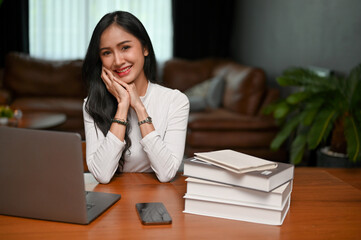 Pretty young Asian female freelancer or businesswoman sits at her desk in her living room