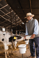 Vertical photo of a farmer giving milk to a calf using a feeding bottle