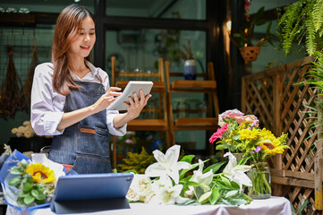 Charming Asian female florist using calculator to calculate the bouquet price.