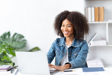 Cheerful african american woman using laptop while sitting on chair in living room