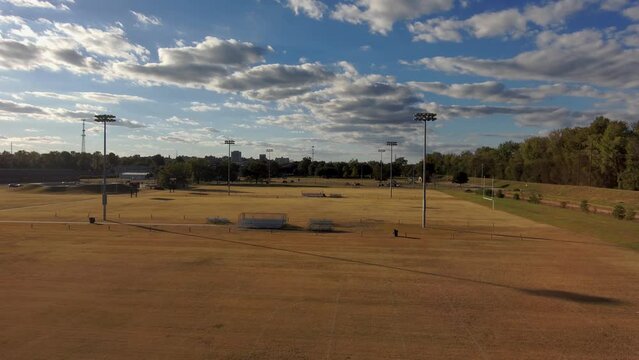 aerial footage of a gorgeous autumn landscape at Carolyn Crayton Park with yellow winter grass and lush green trees kids playing football and a playground with people playing and blue sky with clouds