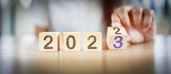 2023 New year concept. Fingers turning the block from 2022 to 2023 by woman's hand. Graphic banner