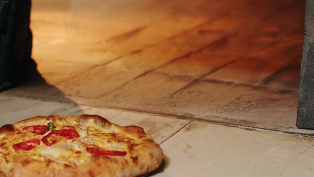 Taking delicious crusty pizza pie out of the hot oven with a wooden shovel. Freshly made pizza margherita baked in traditional stove in a restaurant. Original Italian, Neapolitan food, cuisine.