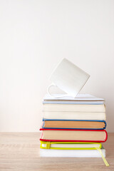 Stack of hardcover books with a white cup of coffee on the top.