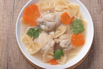 Macaroni soup with chicken thighs in clear broth with carrots.on an rustic old wood background.