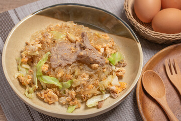Stir fried vermicelli with pork, egg and collard greens in a white plate.