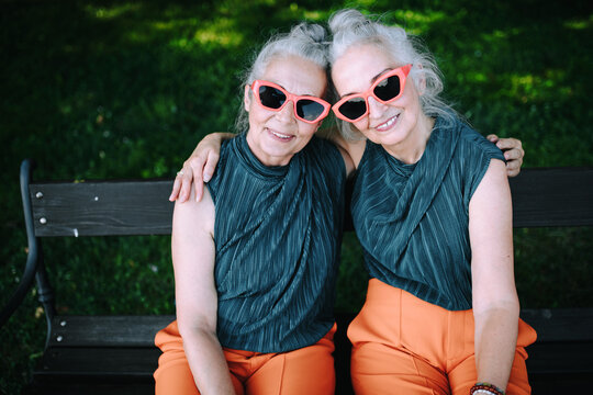 High angle view of happy senior women, twins in same clothes, smiling and posing in city park.