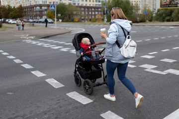 a young mother with a stroller crosses the road at a pedestrian crossing with a cup of coffee in her hands