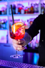Barman in a nightclub holds a glass with an alcoholic cocktail