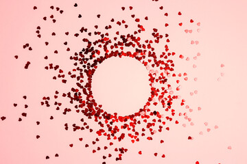 Round frame from red glitter hearts on pink background.