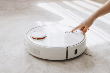Child hand turn on smart robot vacuum cleaner. Modern smart device cleaning floor and carpet. Kid using wireless technology.