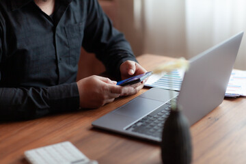 male businessman in black dress Checking his company's last quarter profit secret. using computer, mobile phone and calculator working on brown wooden table, business idea