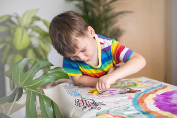 Confident cute male kid art drawing multicolored rainbow arch use paints and brush on table