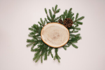 Fototapeta na wymiar Wooden cut with fir branches and cones on beige background. Top view cosmetic podium, stand