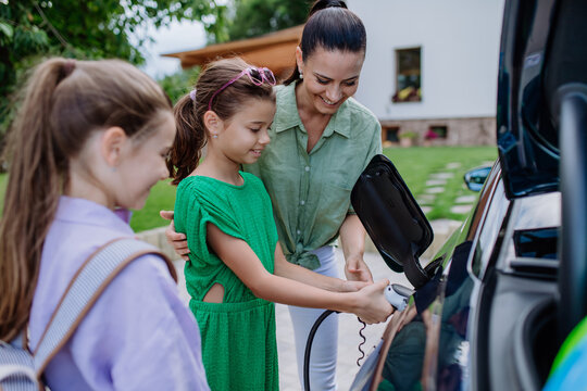 Happy mother showing her little daughters how to charge their electric car.