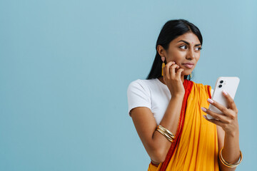 Young beautiful indian woman holding phone and looking aside