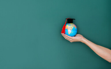 Hand hold a globe and mortarboard in front of blackboard