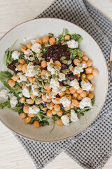 Salad of chickpeas, arugula, cheese, beets, cashews, pumpkin seeds with a dressing of olive oil, freshly ground pepper and salt. White background. Wooden table. Healthy food.
