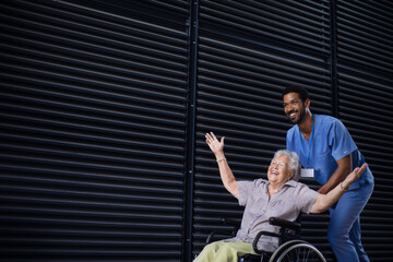 Caregiver man pushing excited senior woman at wheelchair on the street, enjoying time together.