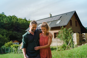 Happy couple standying near their house with solar panels. Alternative energy, saving resources and...