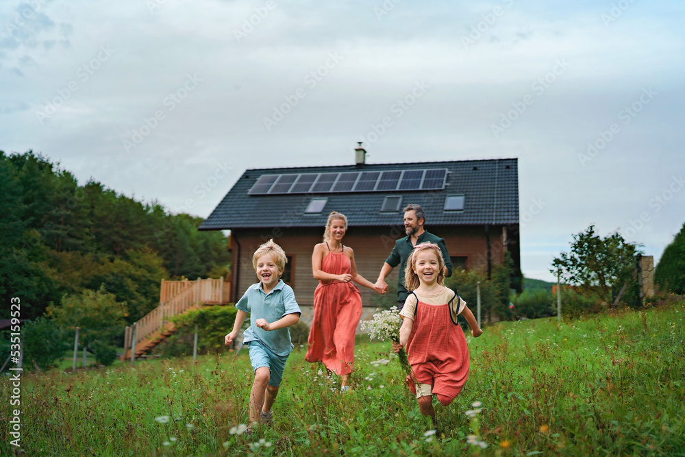 Wall mural Happy family running near their house with solar panels. Alternative energy, saving resources and sustainable lifestyle concept.