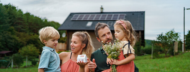 Close up of young family holding paper model of house with solar panels.Alternative energy, saving resources and sustainable lifestyle concept.