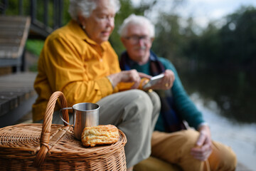 Happy senior couple having picnic and resting near lake after walk.