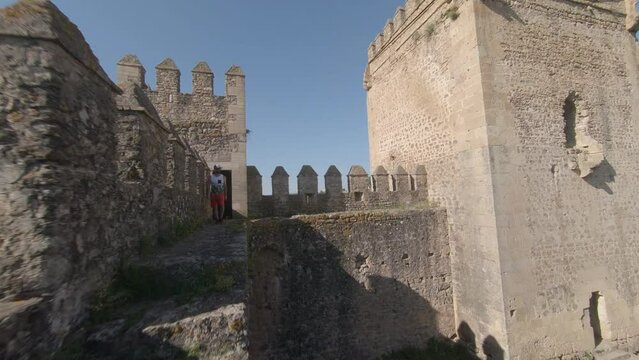 Bearded young man walks along medieval castle wall catwalk, FPV aerial