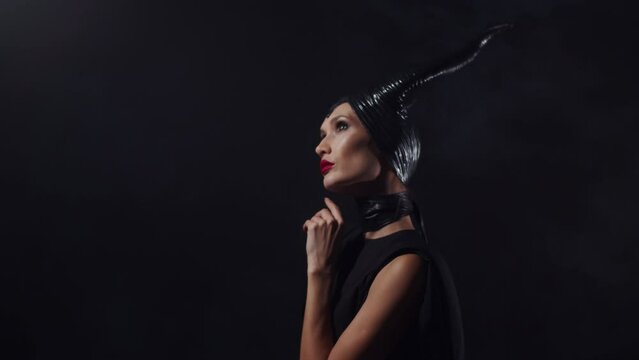 Beautiful woman from a fairytale dressed in black with horns on her head and red lipstick, looking up, thinking, Cartoon, fantasy movie evil villain lady scheming. Cosplay, makeup, dark background