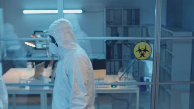 Medium Long Of Three Diverse Doctors In White Hazmat Suits Putting On Face Shields In Laboratory And Walking Away