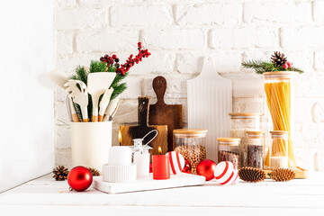 a fragment of a white wooden countertop with various kitchen utensils and Christmas decorations. candles, balls, branches of spruce.