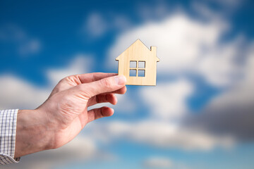 Holds a wooden model of the house in his hand.