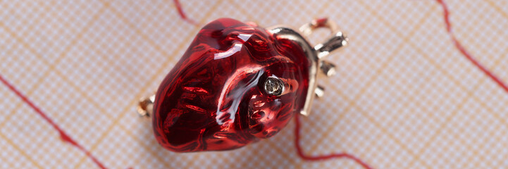 Red glass miniature heart placed over heart cardiogram result paper